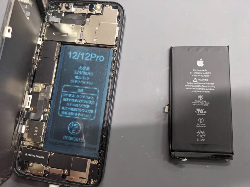 iPhone12へ新品バッテリーを取り付けた交換修理中の様子と取り外した純正バッテリー
